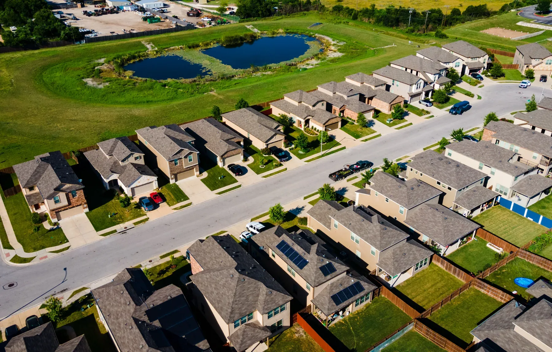 Aerial view of a residential suburban neighborhood featuring new single-family homes with manicured lawns, driveways, and a d