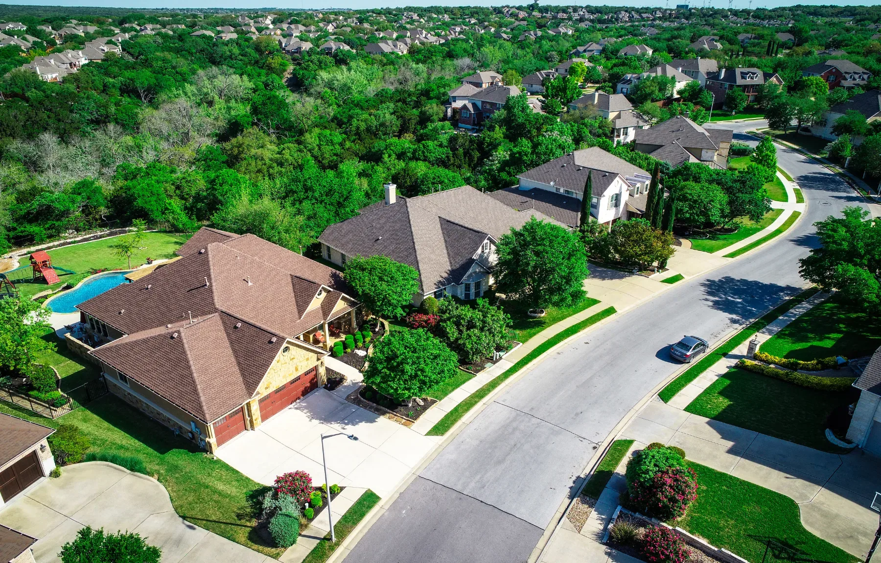 Aerial view of an upscale residential neighborhood featuring well-maintained homes with manicured lawns, mature trees, and a